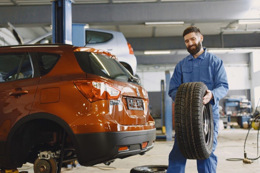Mechaniker trägt einen Reifen durch die Werkstatt